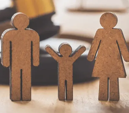 Wooden figures of a family with a child stand in front of a gavel and scales of justice, symbolizing family law and legal matters.