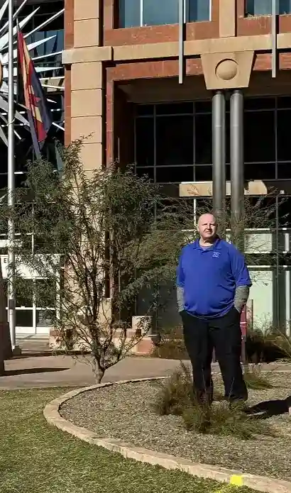 A man stands in front of a building topped with a sun, highlighting a bright and sunny day.