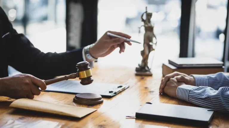Two professionals engaged in a legal discussion with a gavel and Lady Justice statue on a wooden table.