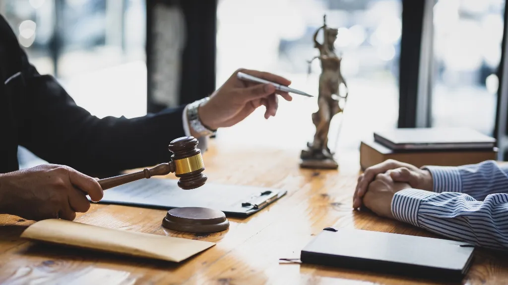 Two professionals engaged in a legal discussion with a gavel and Lady Justice statue on a wooden table.