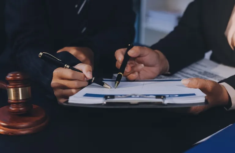 Two individuals in formal attire reviewing and signing documents near a wooden gavel.