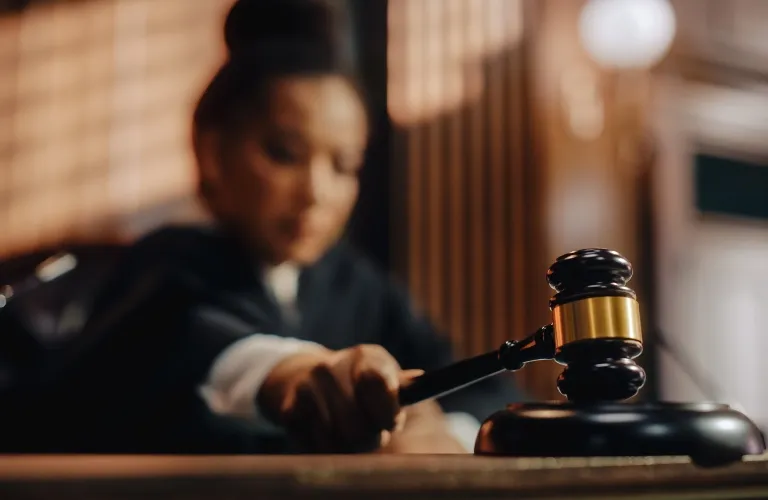 Judge in black robe striking wooden gavel in courtroom with blurred background.