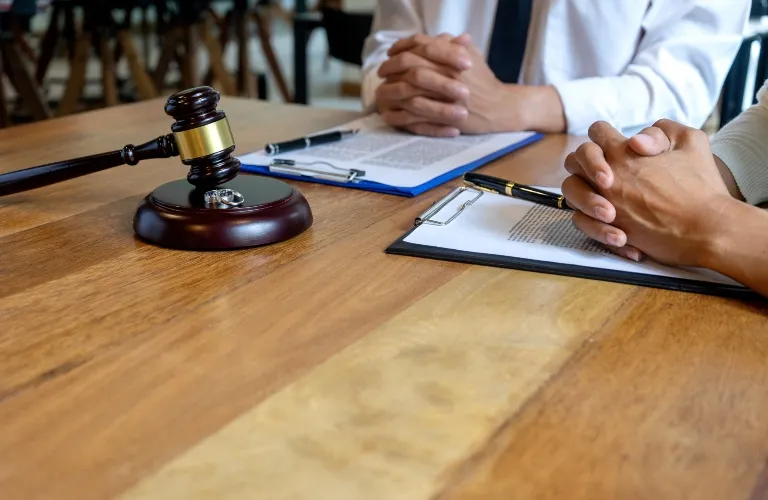Two individuals with clasped hands sitting at a wooden table with legal documents, a pen, and a judge's gavel.