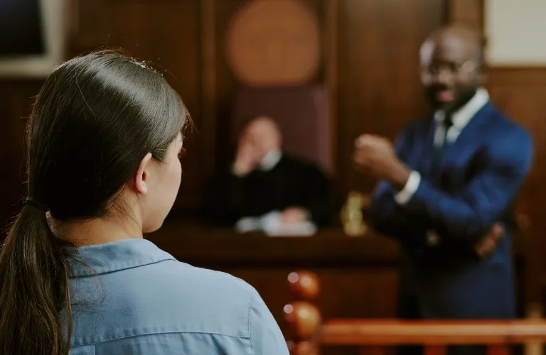 Woman with dark hair in blue shirt facing a lawyer in a blue suit and a judge in a courtroom.