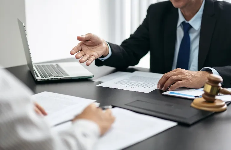 Two professionals in a meeting with documents, a laptop, and a wooden gavel on the table.