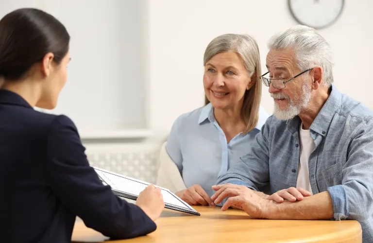 Professional woman consulting with elderly couple at wooden table in bright office.