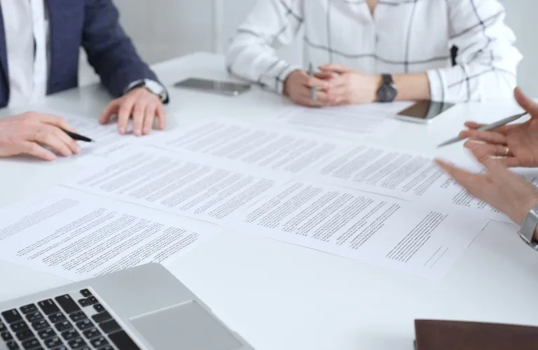 Three professionals reviewing documents on a white table with a laptop and tablets.