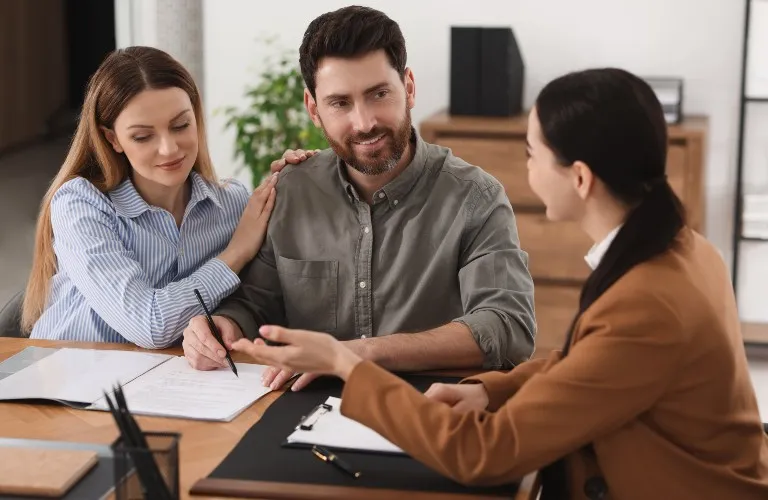 Three adults engaged in a professional discussion at a wooden desk with documents.