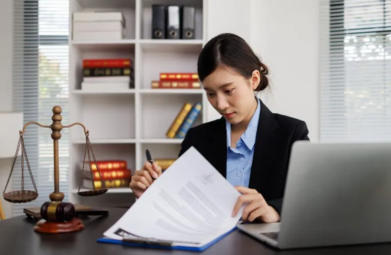 Professional woman in business attire reviewing documents at desk with laptop and legal scales.