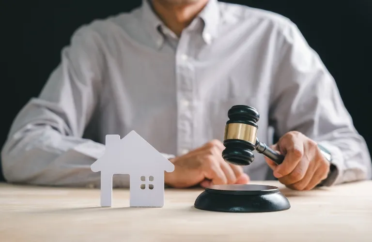 Person holding a gavel near a white house model on a wooden table.