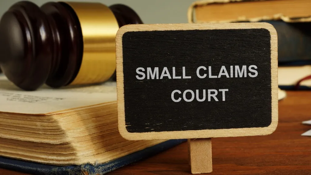 Small wooden sign with "Small Claims Court" text beside a judge's gavel and legal books.