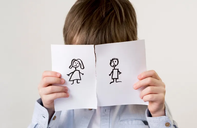 Child holding torn paper with sad stick figure drawings of a boy and a girl.