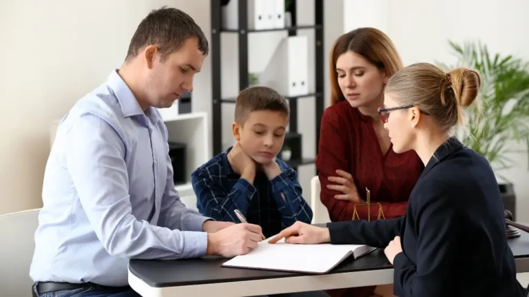 Professional woman in glasses explaining documents to a man, woman, and child at a desk.