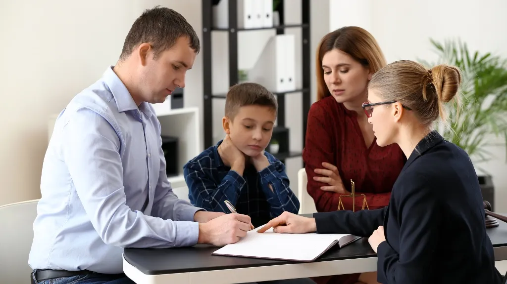 Professional woman in glasses explaining documents to a man, woman, and child at a desk.