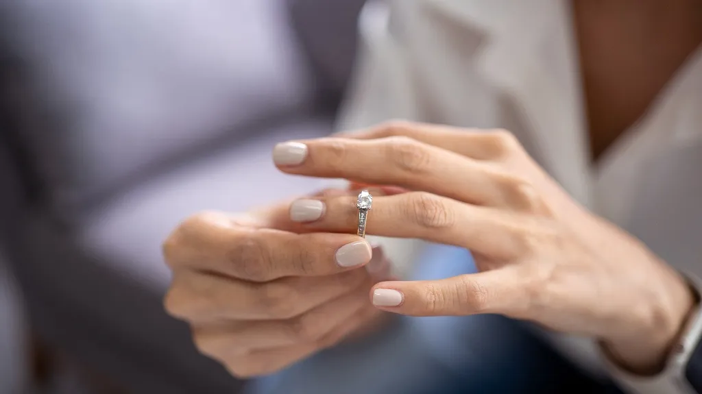Close-up of a person placing a diamond engagement ring on their finger with neutral nail polish.