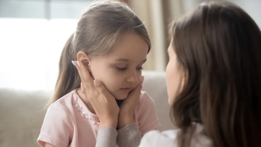 Woman gently holding and comforting a young girl with long hair indoors.
